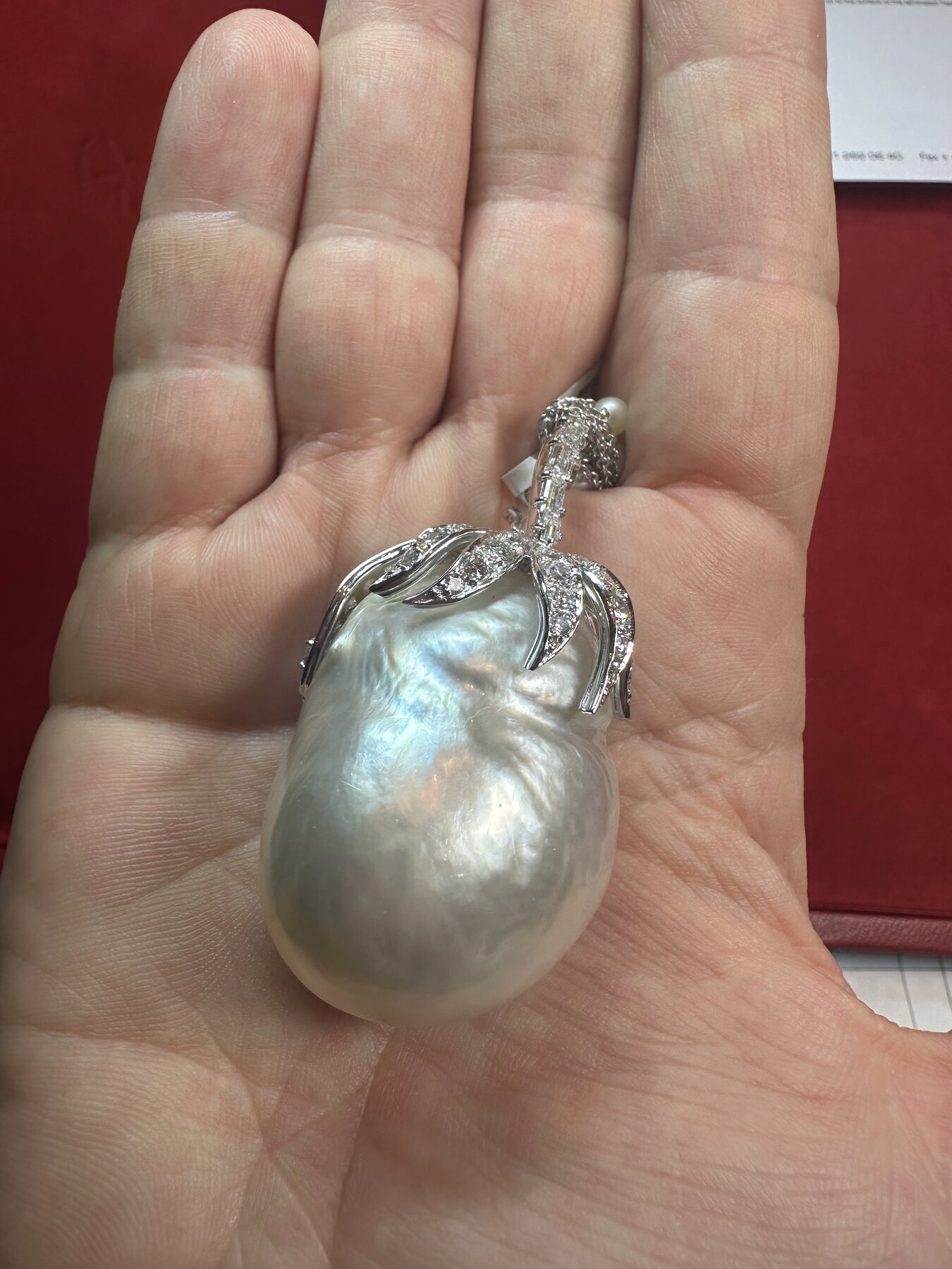 A large baroque natural pearl pendant mounted with a diamond-set floral motif, resting in a palm.